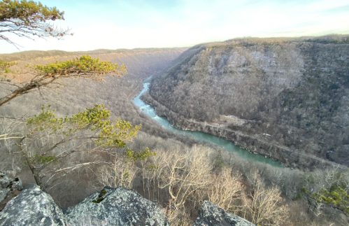 A scenic view of a winding river surrounded by bare trees and steep hills under a clear sky.