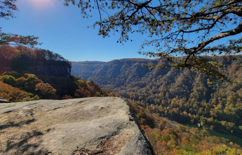 A scenic view from a rocky ledge overlooking a valley filled with autumn foliage and a river below.