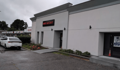 Exterior of a modern building with a sign reading "BREAKOUT," featuring a white car parked nearby.