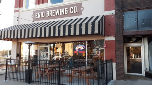 Exterior of Enid Brewing Co. featuring a striped awning, open sign, and outdoor seating area.