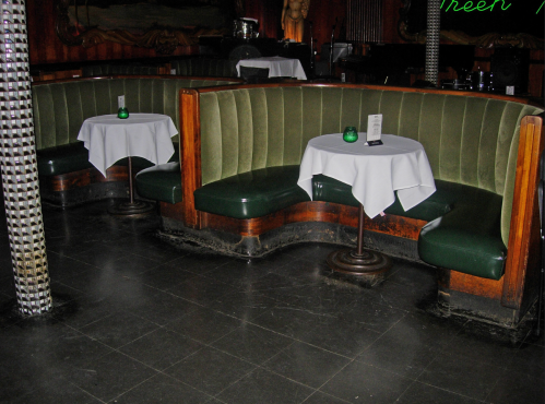 Cozy restaurant seating with green booths and white tablecloths, set in a dimly lit, vintage-style interior.