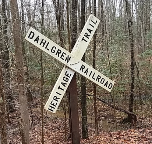 Signpost at a forested intersection, labeled "Dahlgren Trail" and "Heritage Railroad," surrounded by trees.