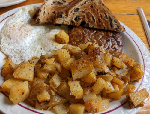 A plate of breakfast featuring two fried eggs, a slice of toast, and seasoned diced potatoes.