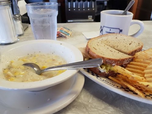 A bowl of corn chowder, a sandwich on whole grain bread, and a plate of waffle fries with a glass of water and coffee.