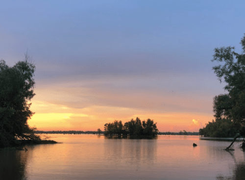 A serene lake at sunset, with soft colors reflecting on the water and trees lining the shore.