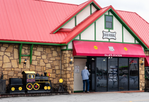 A stone building with a red roof and awning, featuring a train decoration outside and a sign for Ollie's Station.