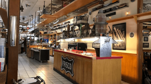 A cozy diner interior featuring a counter, vintage decor, and model trains on display above.