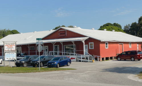 A red antique mall building with a white roof, surrounded by parked cars and greenery under a clear blue sky.