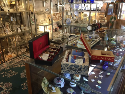 A display of various antiques and collectibles, including glassware, jewelry boxes, and decorative items.