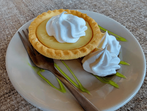 A small tart with a creamy filling topped with whipped cream, served on a plate with two dollops of whipped cream.