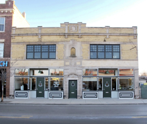 Historic brick building with large windows and decorative facade, featuring two storefronts on a city street.