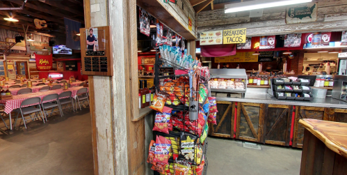 Interior of a rustic eatery featuring a snack rack, seating area, and a menu board for breakfast tacos.