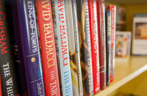 A close-up of a bookshelf filled with various books, featuring titles by David Baldacci and others.