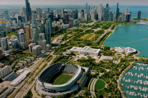 Aerial view of Chicago's skyline, parks, and Lake Michigan, featuring a stadium and marina along the waterfront.