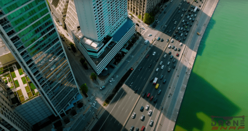 Aerial view of a busy city street with cars, tall buildings, and a green river beside the road.