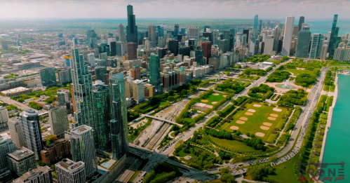 Aerial view of a vibrant city skyline with green parks and a lake in the foreground.