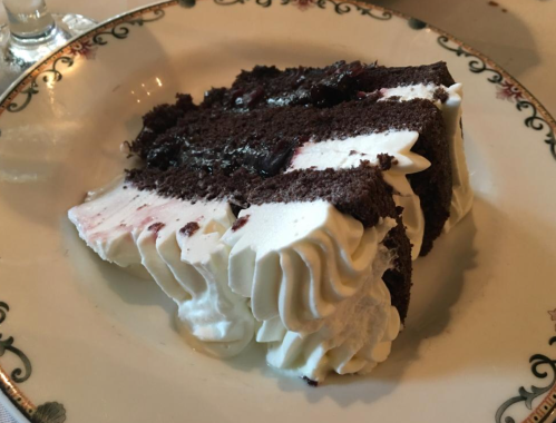 A slice of chocolate cake with white frosting on a decorative plate.