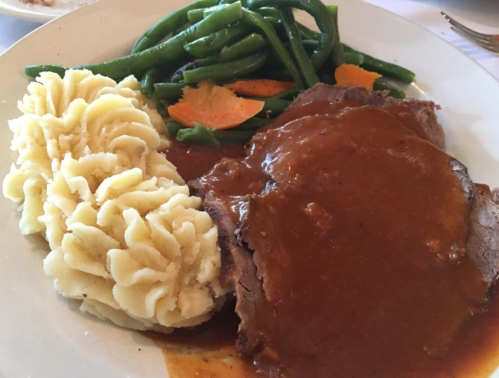 A plate of sliced roast beef with gravy, mashed potatoes, green beans, and carrots.