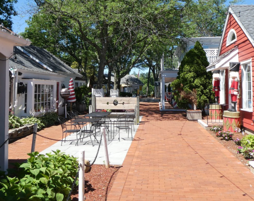 Charming outdoor pathway lined with colorful buildings, greenery, and patio seating in a quaint village setting.