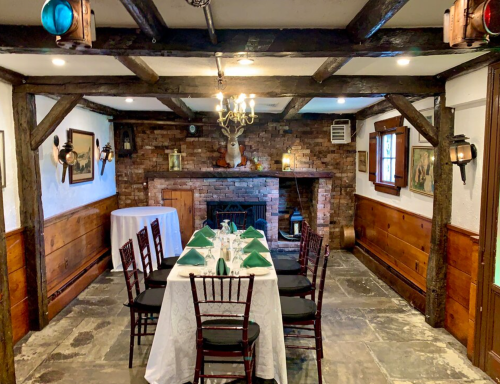 Cozy dining room with a wooden beam ceiling, a fireplace, and a table set for a meal. Rustic decor and warm lighting.