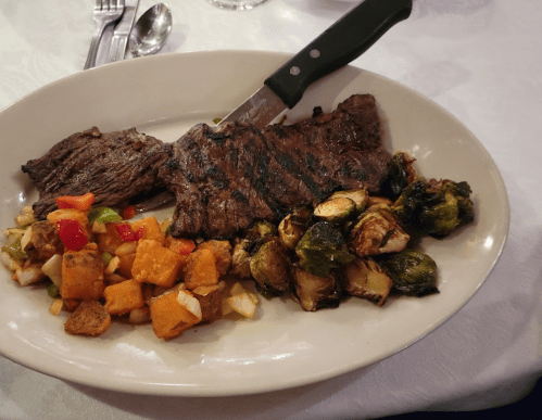A plate with grilled steak, roasted Brussels sprouts, and a colorful vegetable medley.