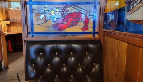 A cozy restaurant booth with a stained glass lobster design on the wall and wooden paneling in the background.