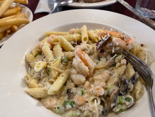 A plate of creamy pasta with shrimp, mushrooms, and herbs, served with a side of fries.