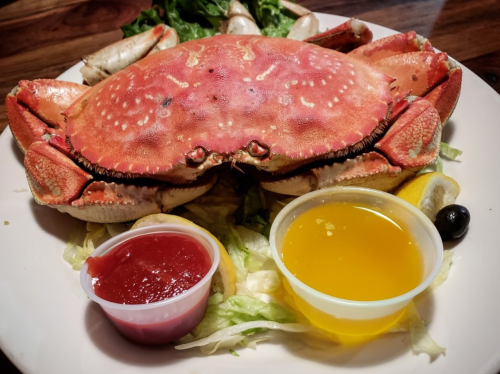 A whole cooked crab on a plate, surrounded by lettuce, with two dipping sauces and a lemon wedge.