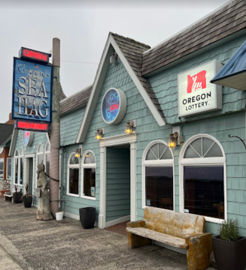 Exterior of a coastal restaurant with a blue-green facade, featuring signs for "Green's Sea Hag" and the Oregon Lottery.