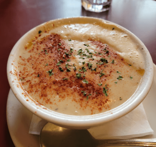 A bowl of creamy soup topped with herbs and spices, served on a plate with a spoon beside it.
