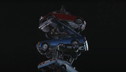 A stack of four cars piled on top of each other against a dark background.
