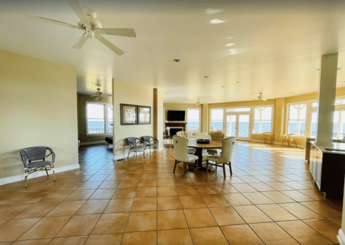 Spacious, sunlit living area with tile flooring, ceiling fans, and large windows offering a view.