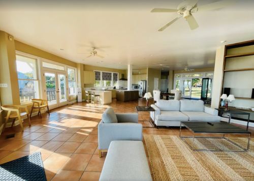 Bright, spacious living area with a modern kitchen, large windows, and comfortable seating. Natural light fills the room.