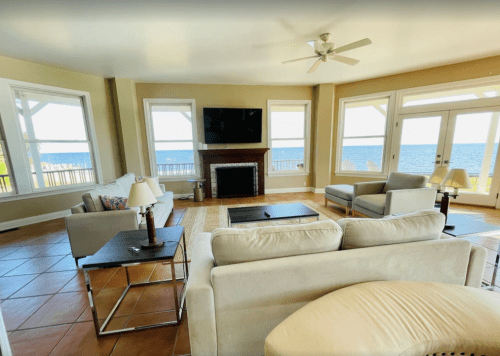Bright living room with large windows overlooking the water, featuring a TV, sofas, and a coffee table.
