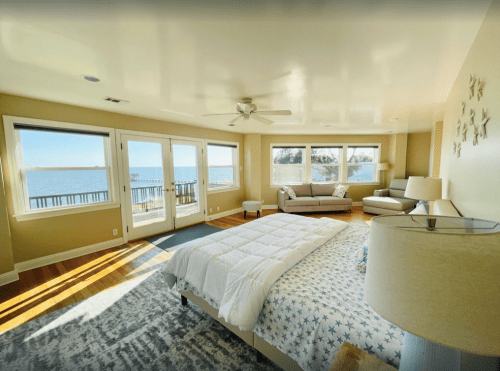 Bright, spacious bedroom with a large bed, seating area, and windows overlooking a scenic waterfront view.