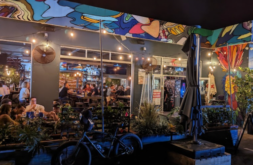 A vibrant restaurant with colorful murals, outdoor seating, and patrons enjoying their meals in a lively atmosphere.