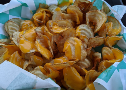 A basket of crispy potato chips topped with melted cheese sauce, served in a green and white checkered paper.