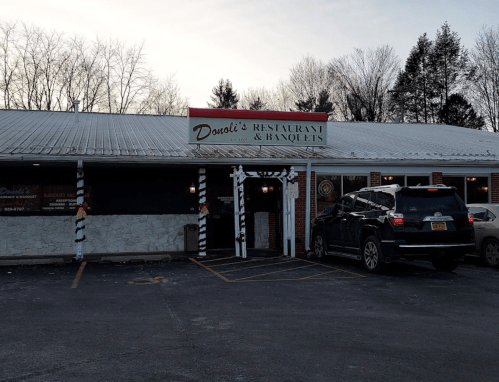 Exterior of Doolie's Restaurant & Banquets, featuring a sign and parked car, surrounded by trees.