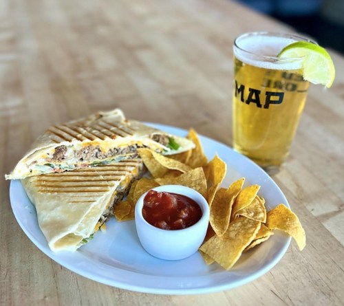 A plate with a grilled quesadilla, tortilla chips, salsa, and a glass of beer with a lime wedge.