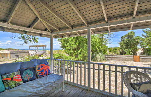 Cozy porch with colorful cushions, overlooking a sandy beach and lush greenery under a clear blue sky.