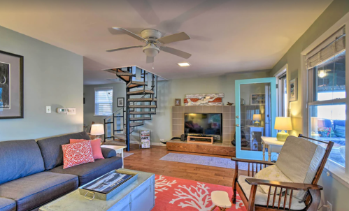 Cozy living room with a gray sofa, spiral staircase, fireplace, and large windows, featuring warm lighting and decor.
