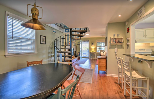 A cozy dining area with a round table, spiral staircase, and open living space filled with natural light.