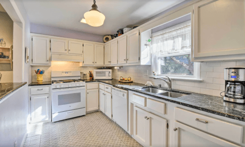 Bright kitchen with white cabinets, granite countertops, a stove, microwave, and coffee maker, featuring a window with natural light.