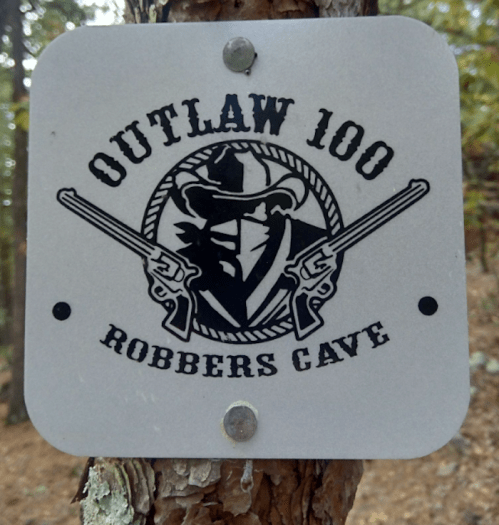 Sign featuring "Outlaw 100" with crossed revolvers and a cowboy silhouette, labeled "Robbers Cave."