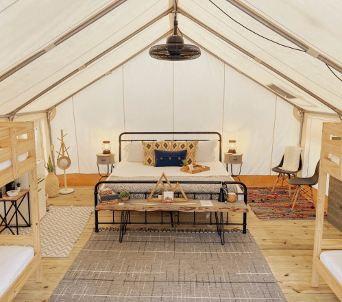 Cozy glamping tent interior with a double bed, wooden furniture, and decorative accents. Warm, inviting atmosphere.