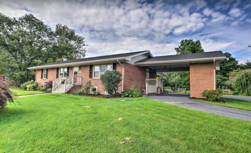 A brick house with a front porch, green lawn, and a carport under a partly cloudy sky.