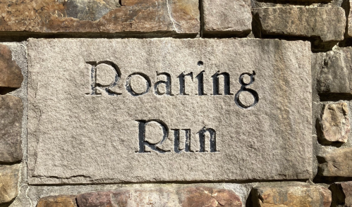 Stone sign reading "Roaring Run" on a textured stone wall.