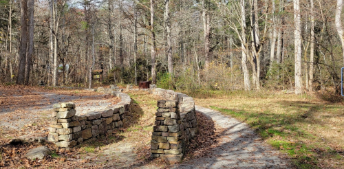 A winding gravel path surrounded by trees and stone walls in a wooded area during autumn.