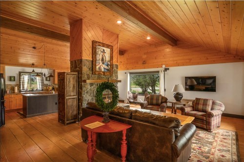 Cozy living room with wooden beams, stone fireplace, and a view of the kitchen, featuring comfortable seating and decor.