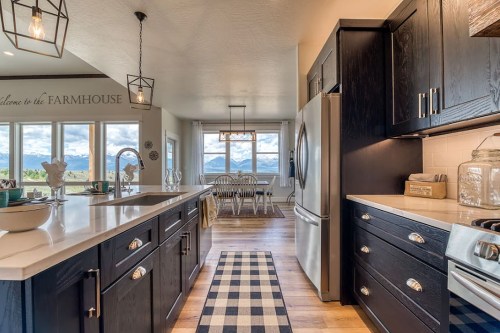 Modern kitchen with dark cabinets, white countertops, and a view of mountains through large windows. Cozy dining area visible.